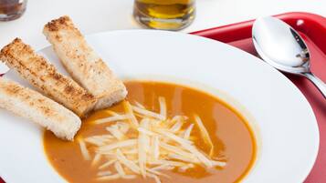 Un plato blanco con un bol de sopa, dos rebanadas de pan tostado y queso rallado sobre un mantel rojo.