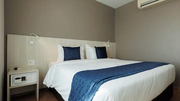 A hotel room with a bed, nightstand, and wall-mounted air conditioner.