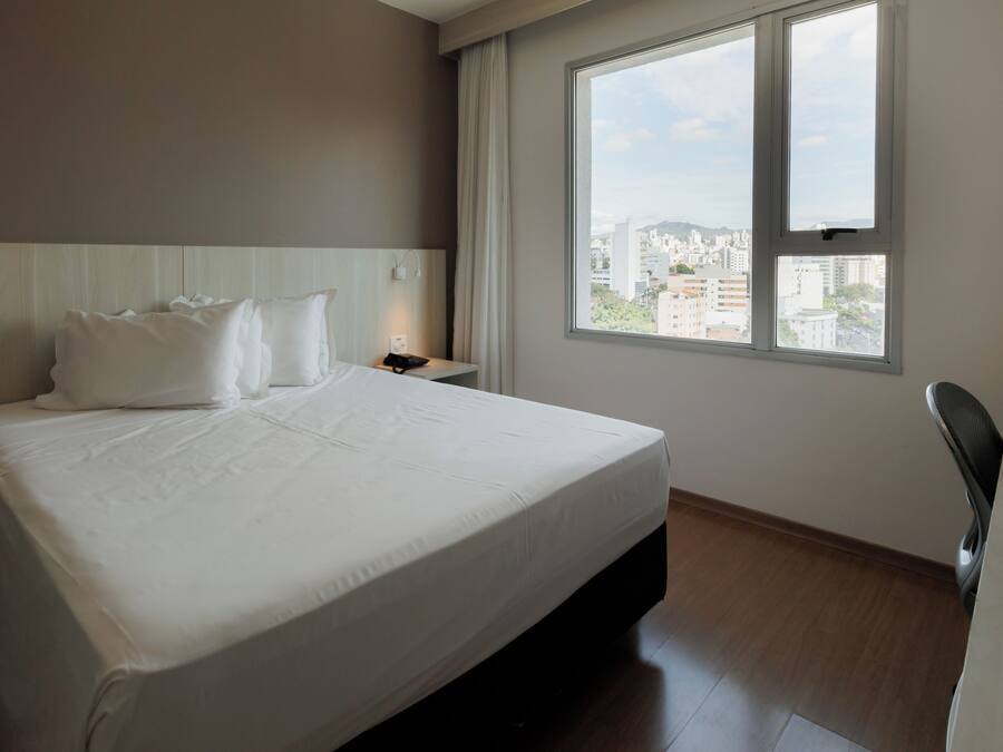 A hotel room with a large bed, a desk, and a window with a city view.