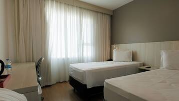 A hotel room with two beds, a desk with a chair, a mirror, and a window with curtains.