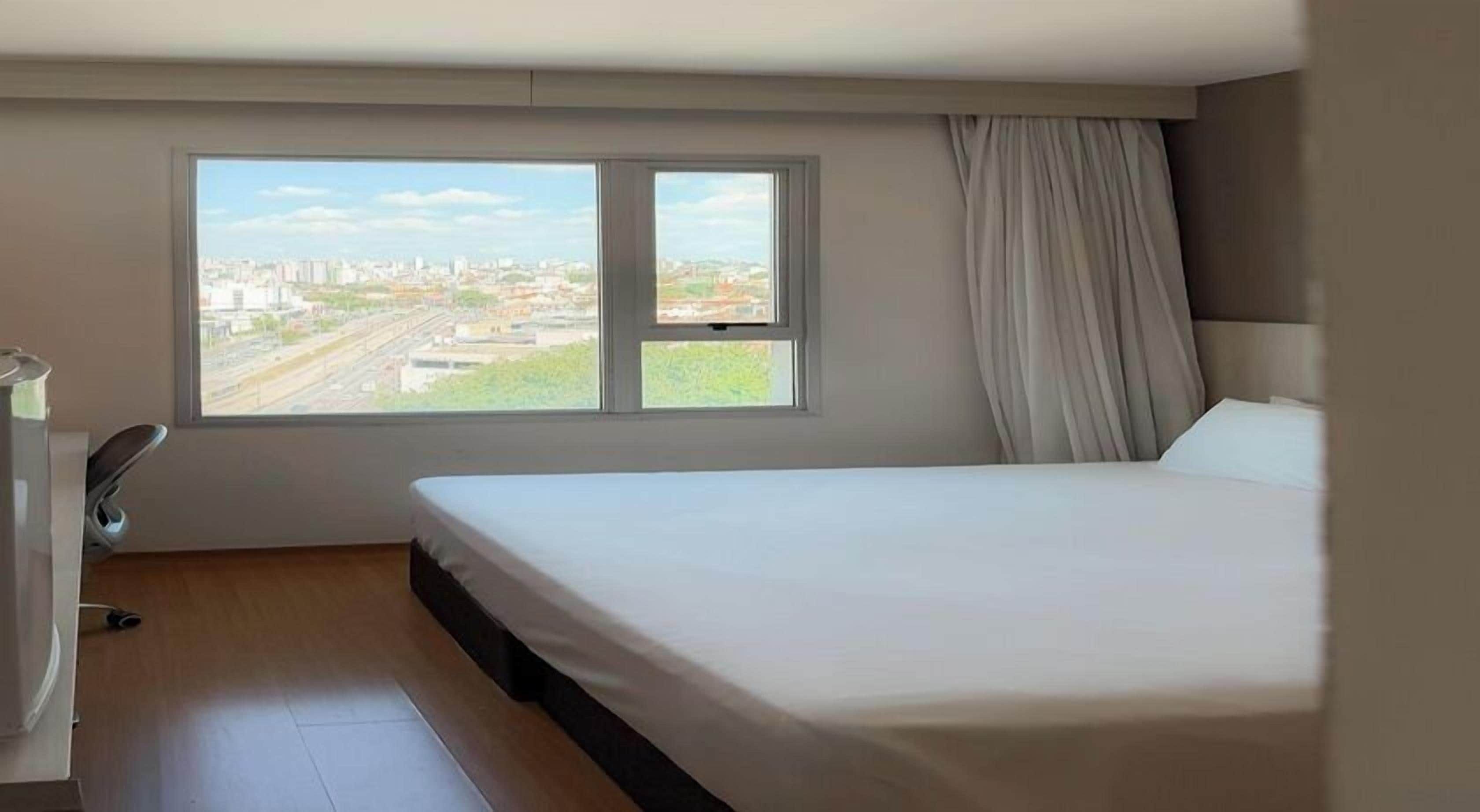 Habitación de hotel con cama, escritorio y ventana con vistas a la ciudad.