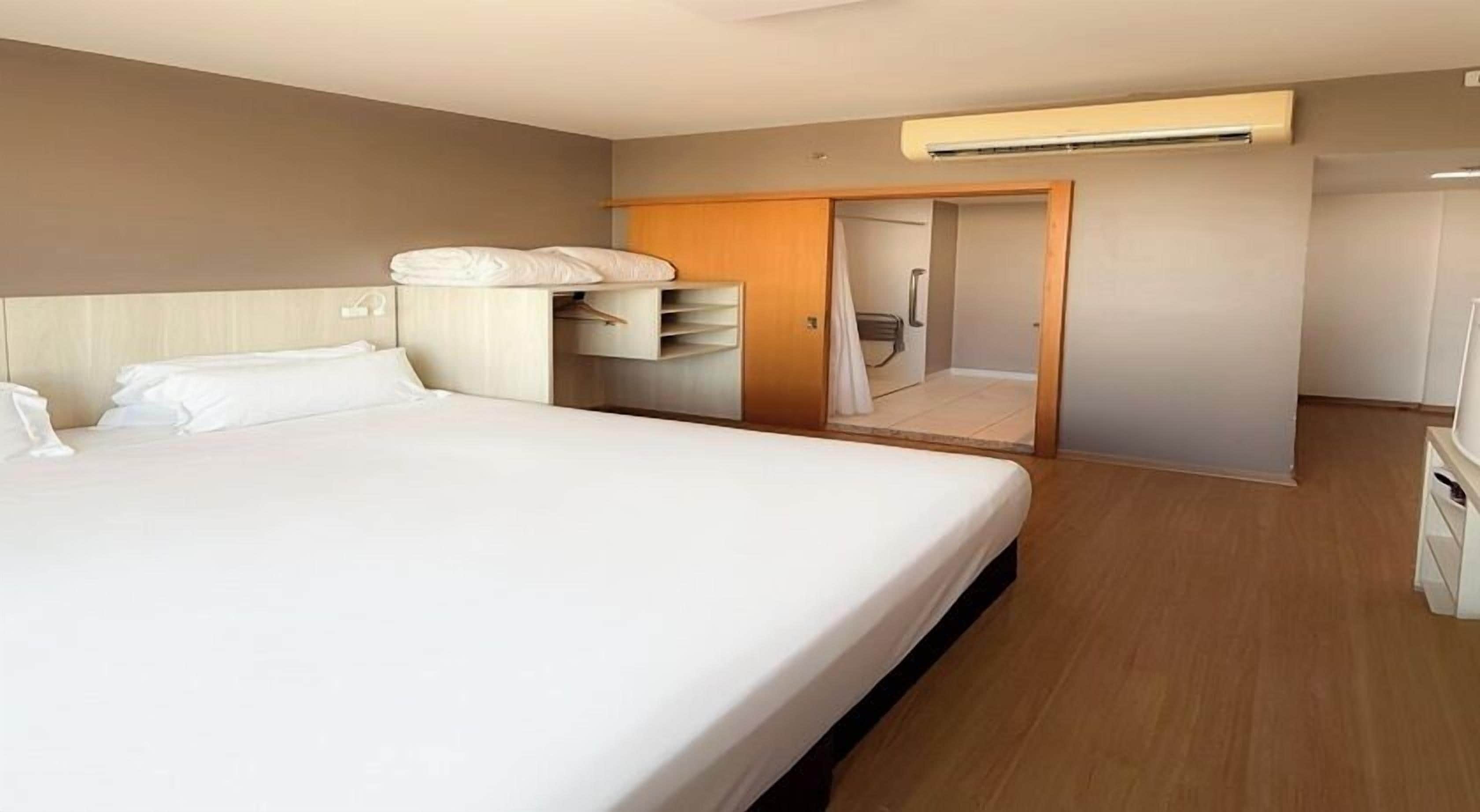 Habitación de hotel con una cama grande, un armario, un escritorio y un espejo.