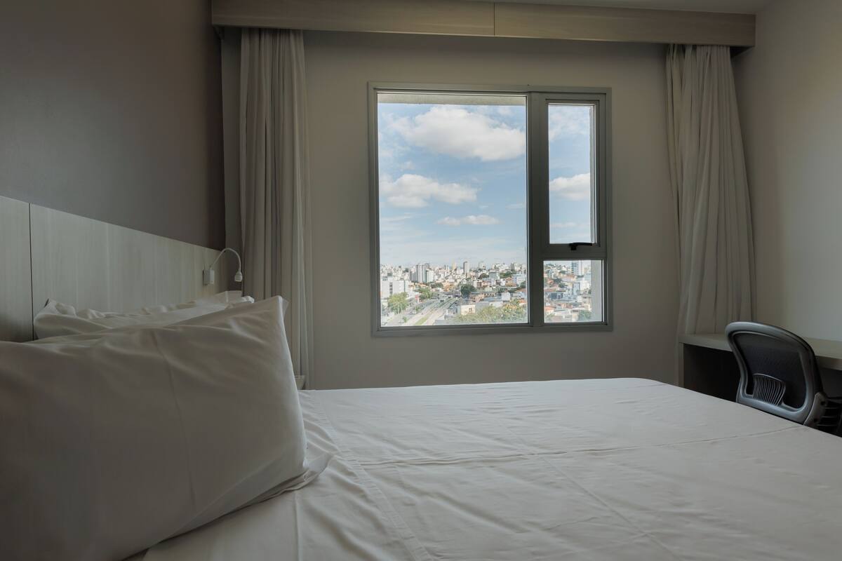 Una habitación de hotel con cama, una silla y ventana con vistas a la ciudad.