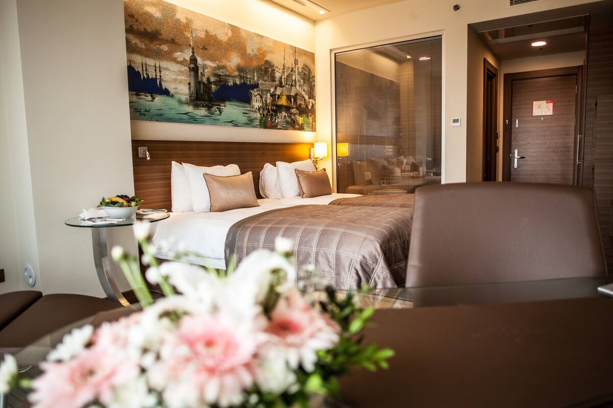 A hotel room with a large bed, a sitting area, a small table with a vase of flowers, and a painting on the wall.