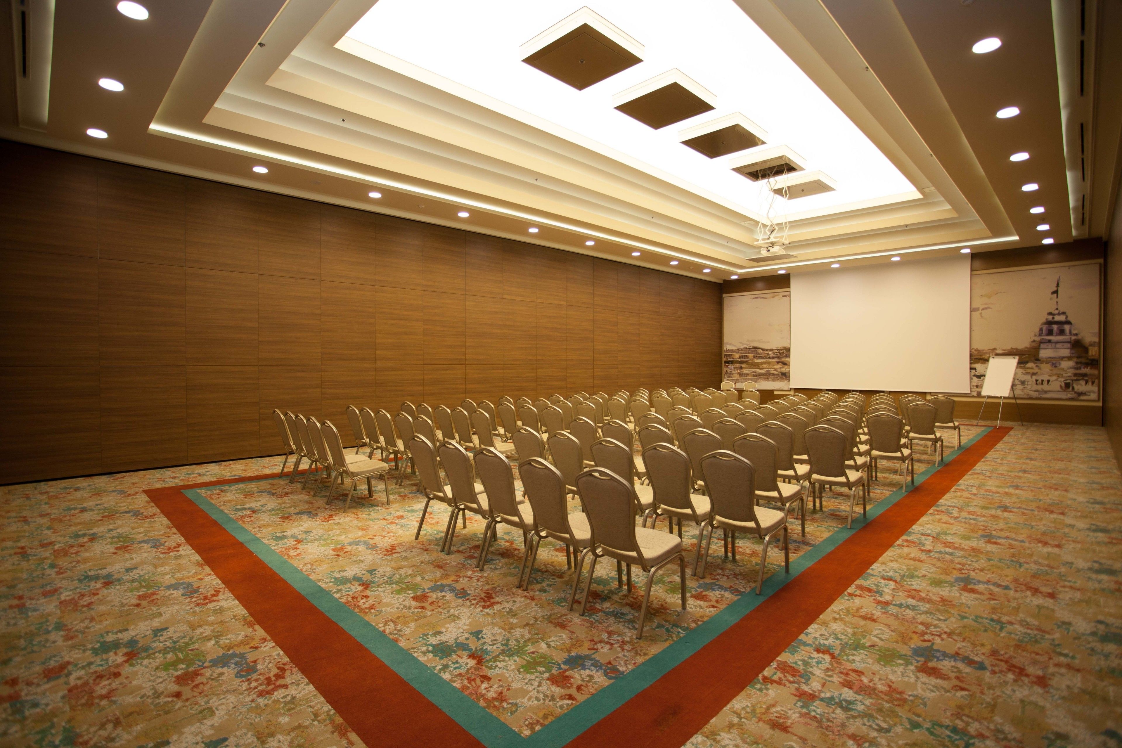 A conference room with rows of chairs, a projector screen, and a wooden wall.