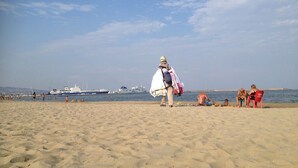 Una playa arenosa con gente y barcos al fondo.