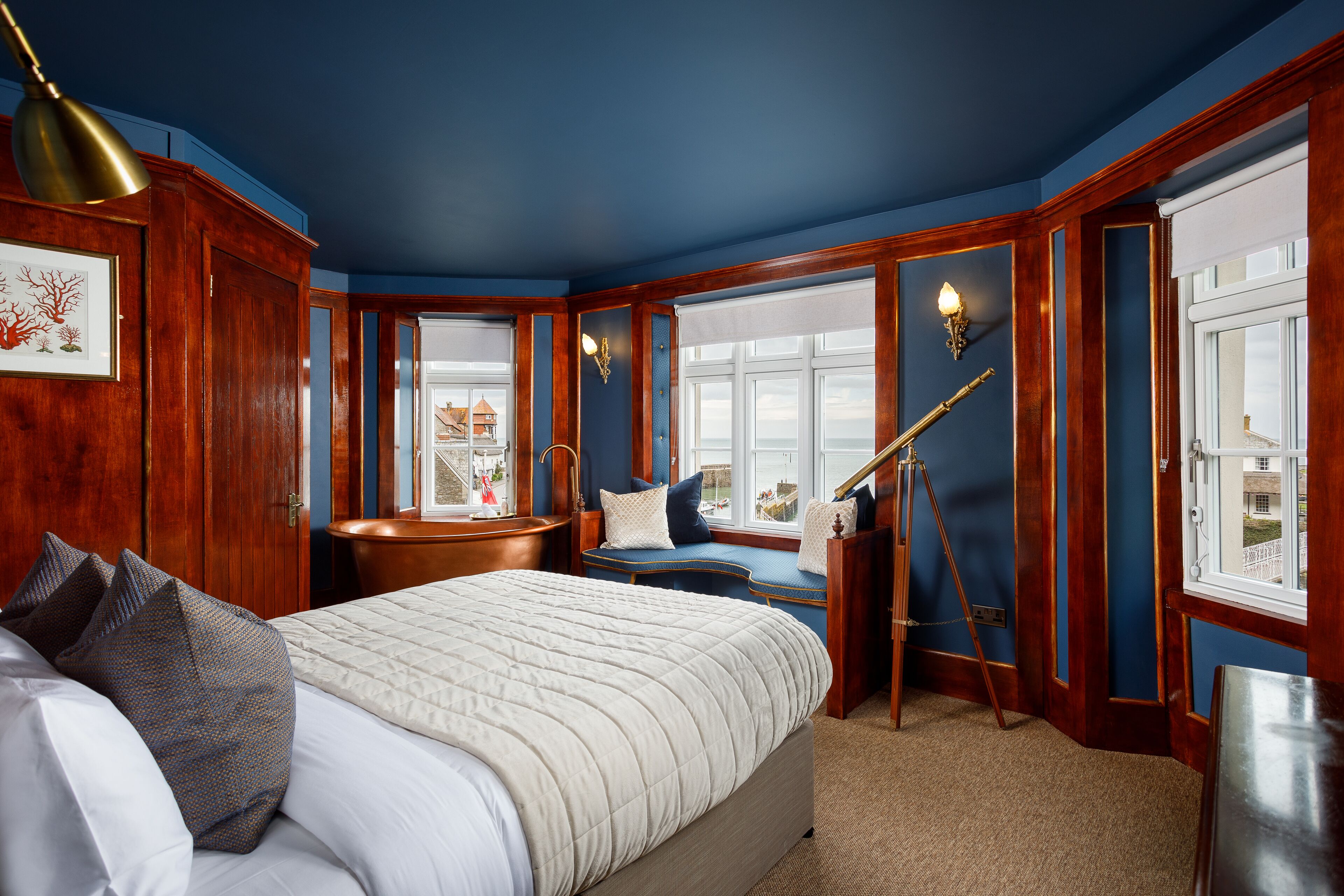 A bedroom with a large bed, a wooden bench, a telescope, and a view of a building through the window.