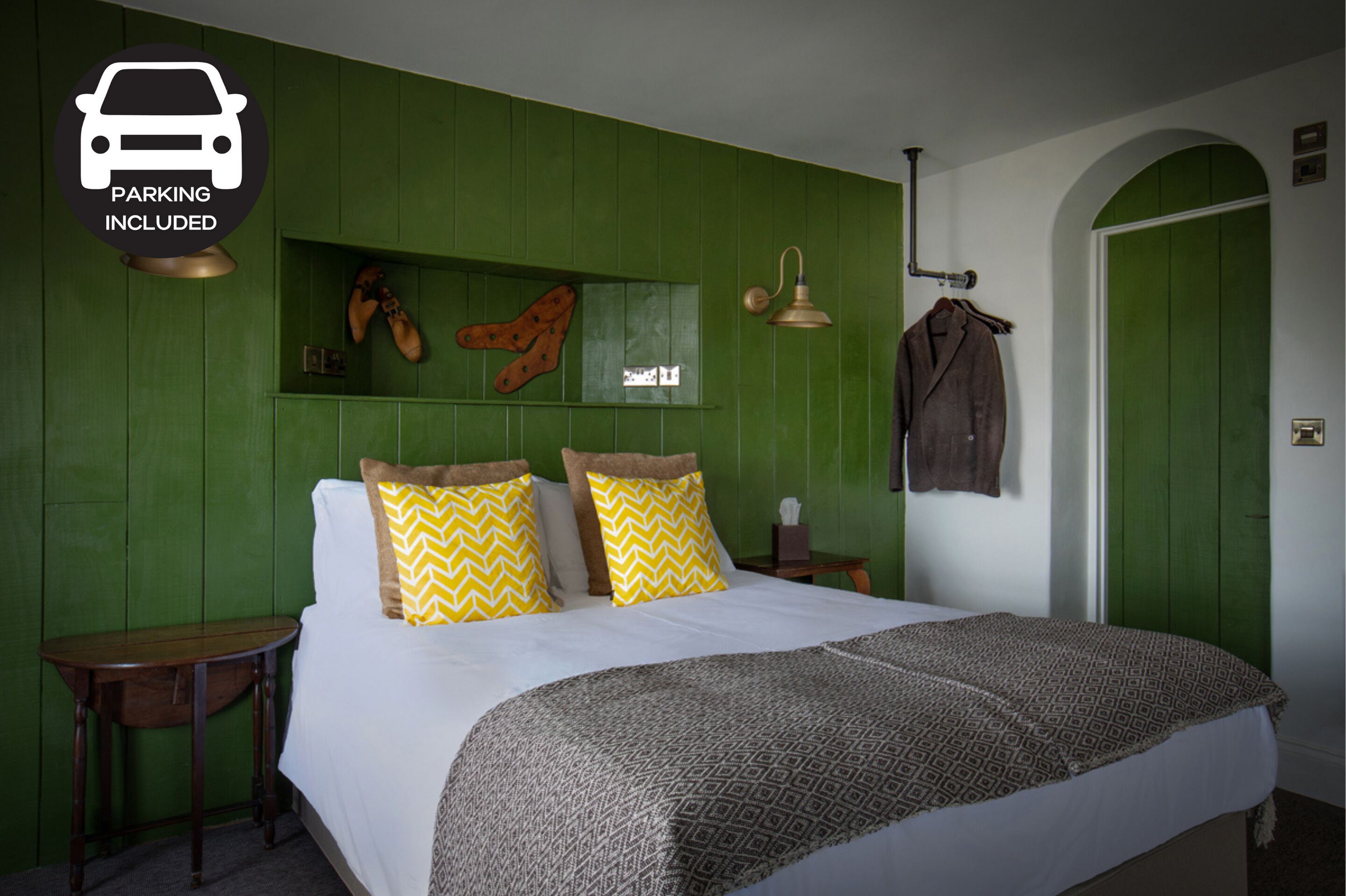 A bedroom with a green wall, a bed with patterned bedding, a coat hanging on the wall, and a sign indicating parking is included.