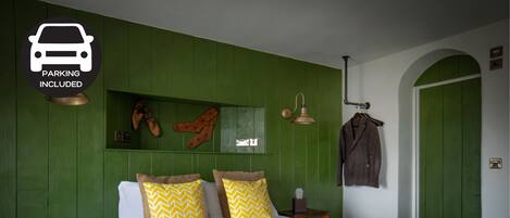 A bedroom with a green wall, a bed with patterned bedding, a coat hanging on the wall, and a sign indicating parking is included.