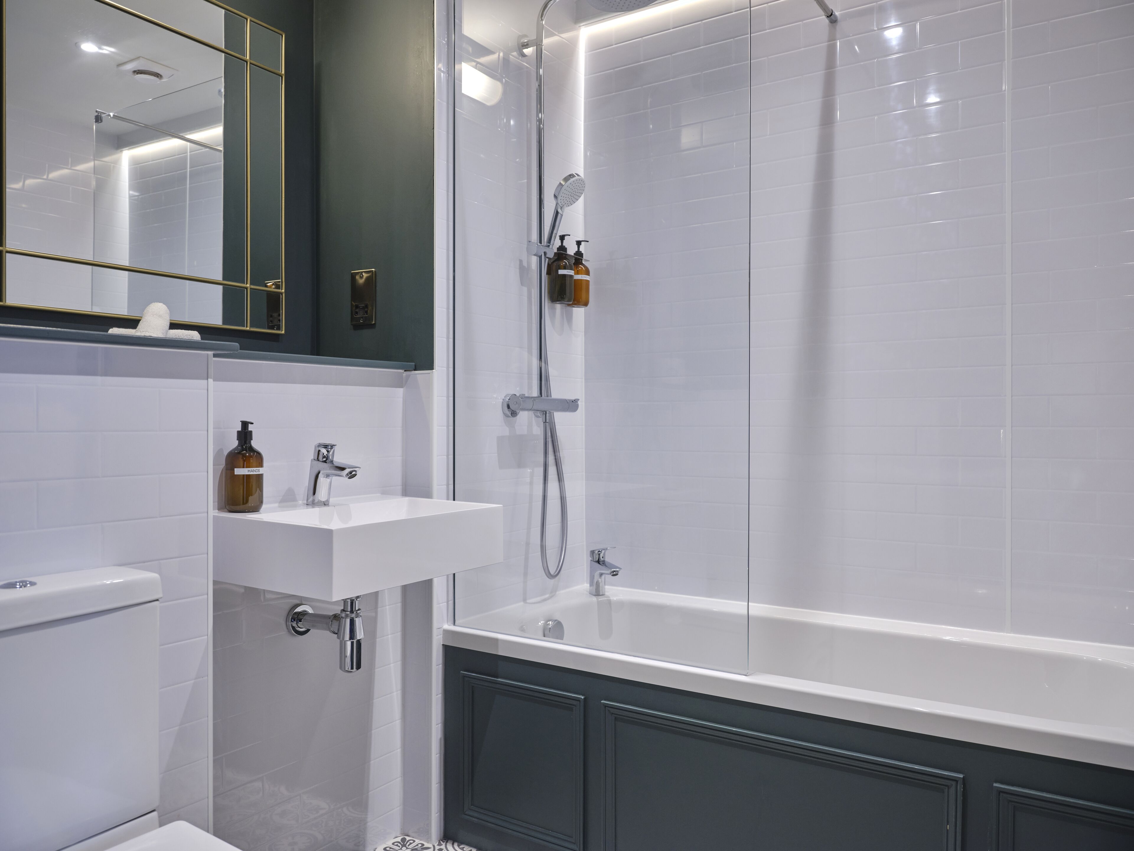 Een moderne badkamer met een douchecabine van glas, een wit wastafelmeubel met een zeepdispenser en een toilet.