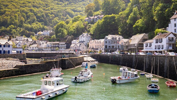 Un port où des bateaux sont amarrés, entouré de maisons et bordé par une colline.
