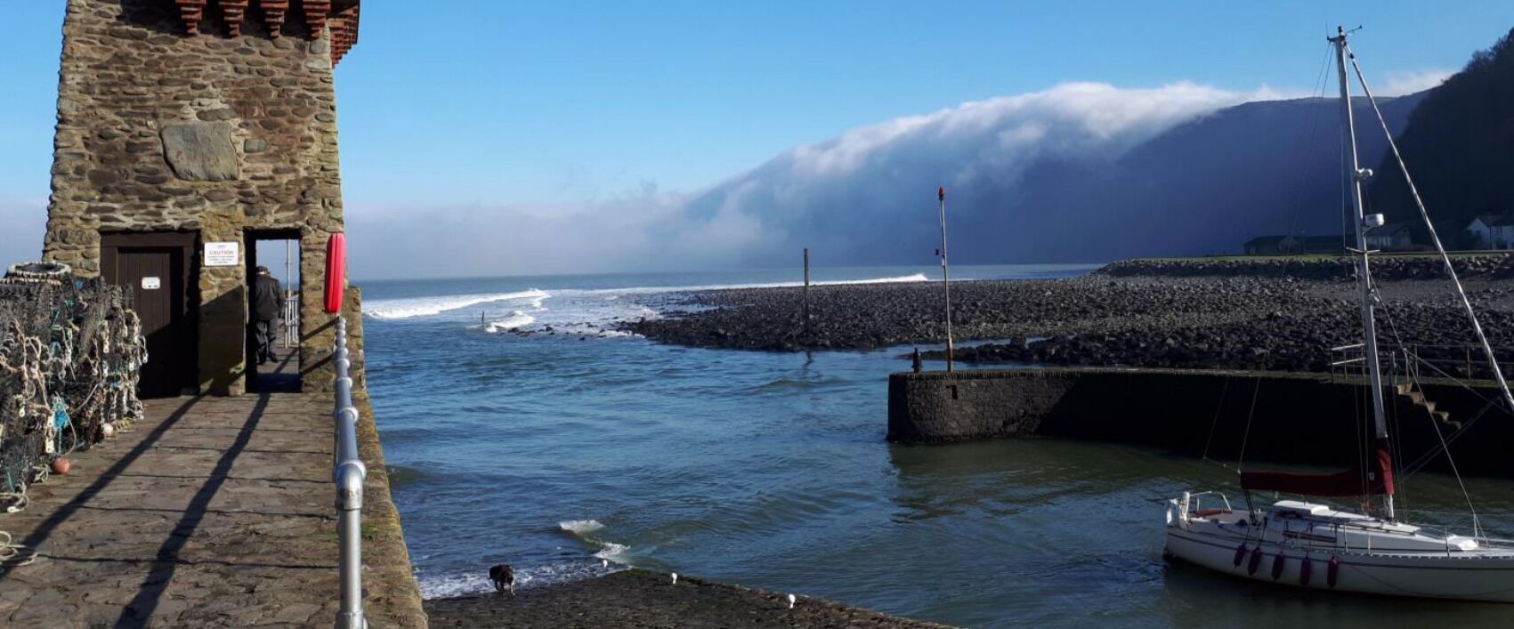 A coastal scene with a stone tower, a rocky breakwater, and a boat docked near the shore.