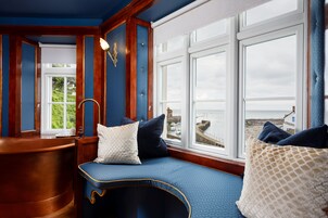 Una habitación con un banco de madera curvado, vista al mar y ventana con vista al puerto.