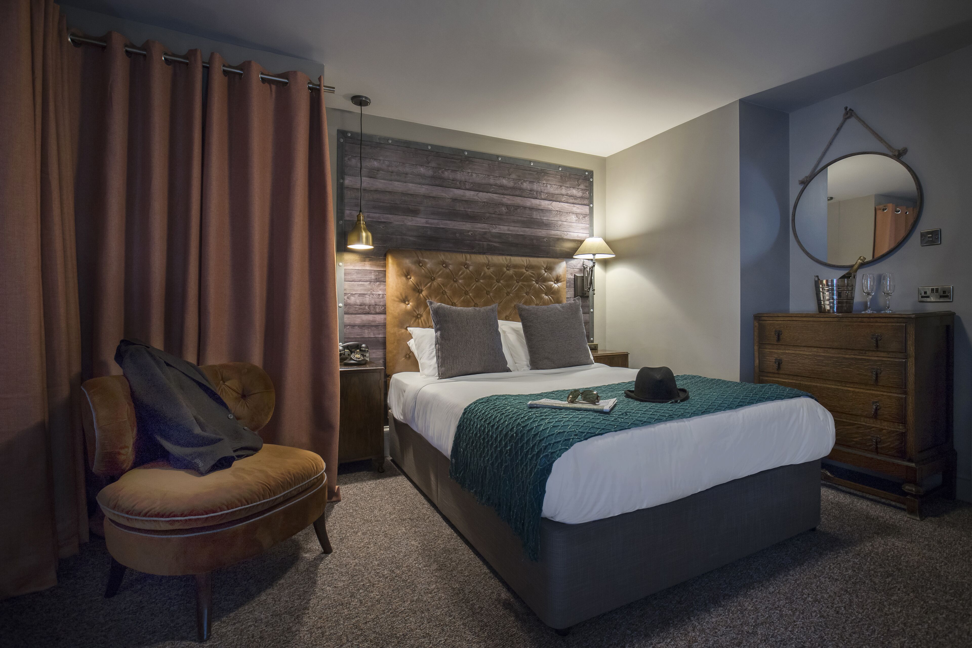 A hotel room with a large bed, a wooden headboard, a nightstand, a dresser, a chair, and a mirror on the wall.