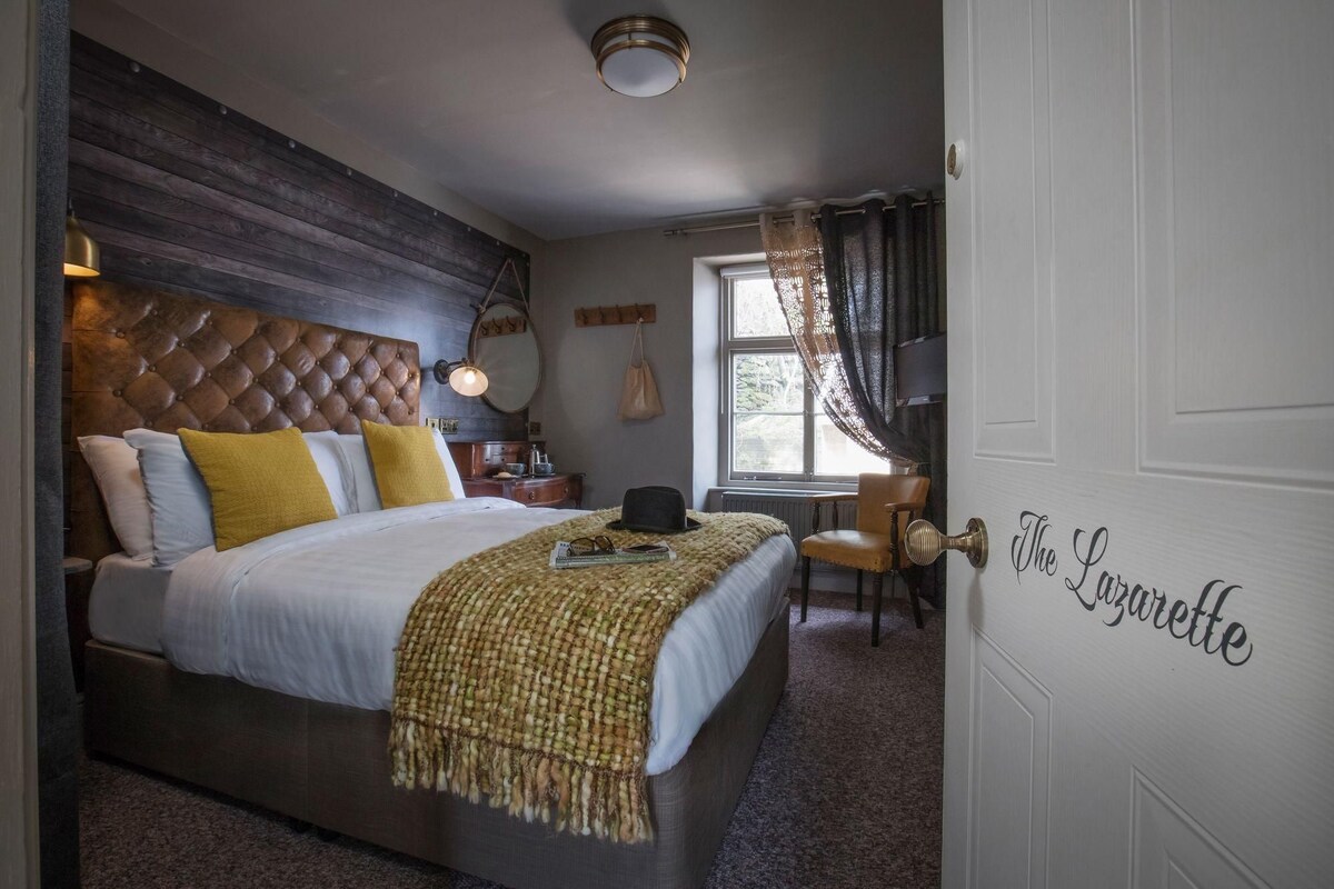 Une chambre à coucher avec un grand lit, une tête de lit en bois, une table de chevet, une lampe, une chaise et une fenêtre avec des rideaux.