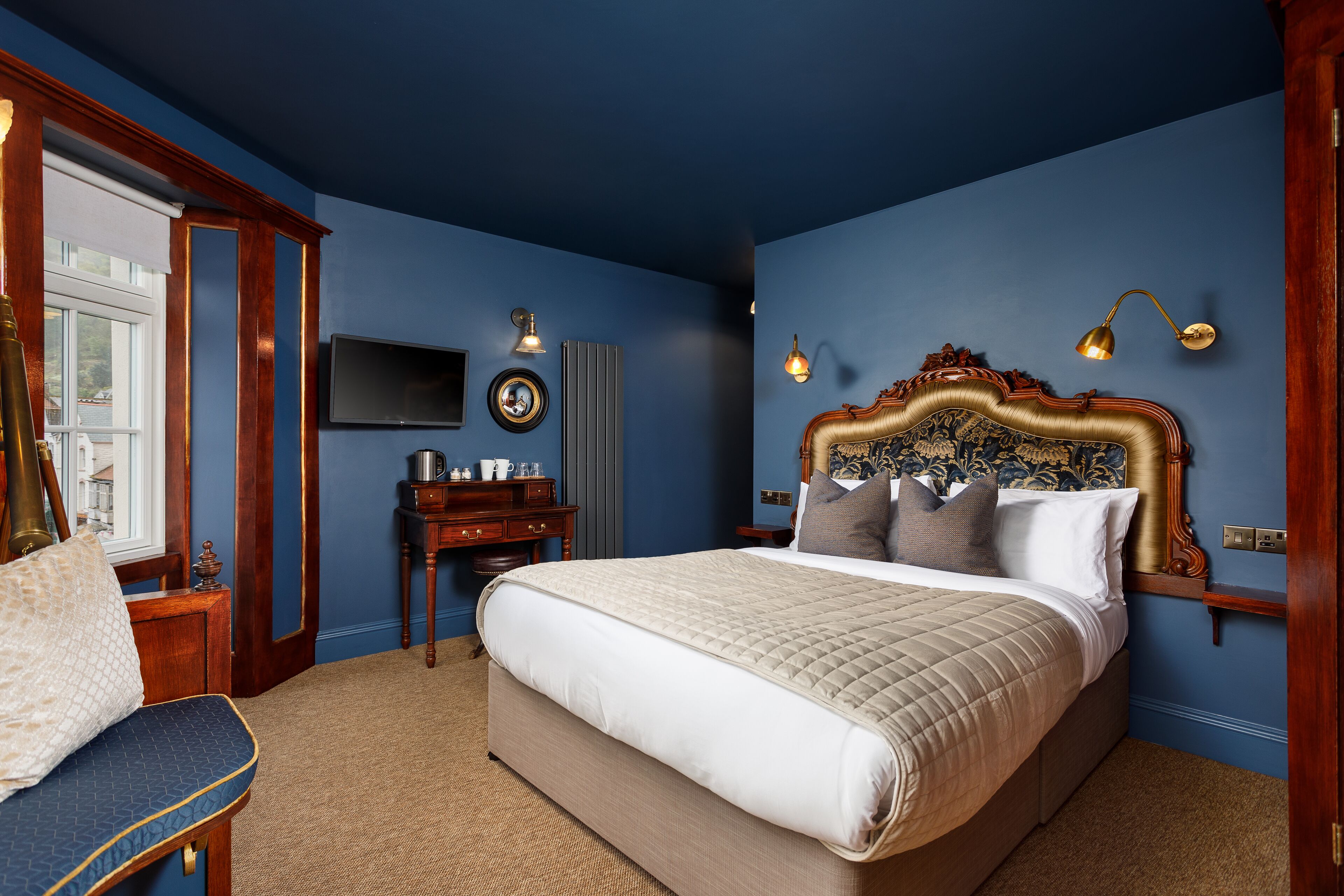 A bedroom with a large bed, a desk, a chair, and a TV on the wall.