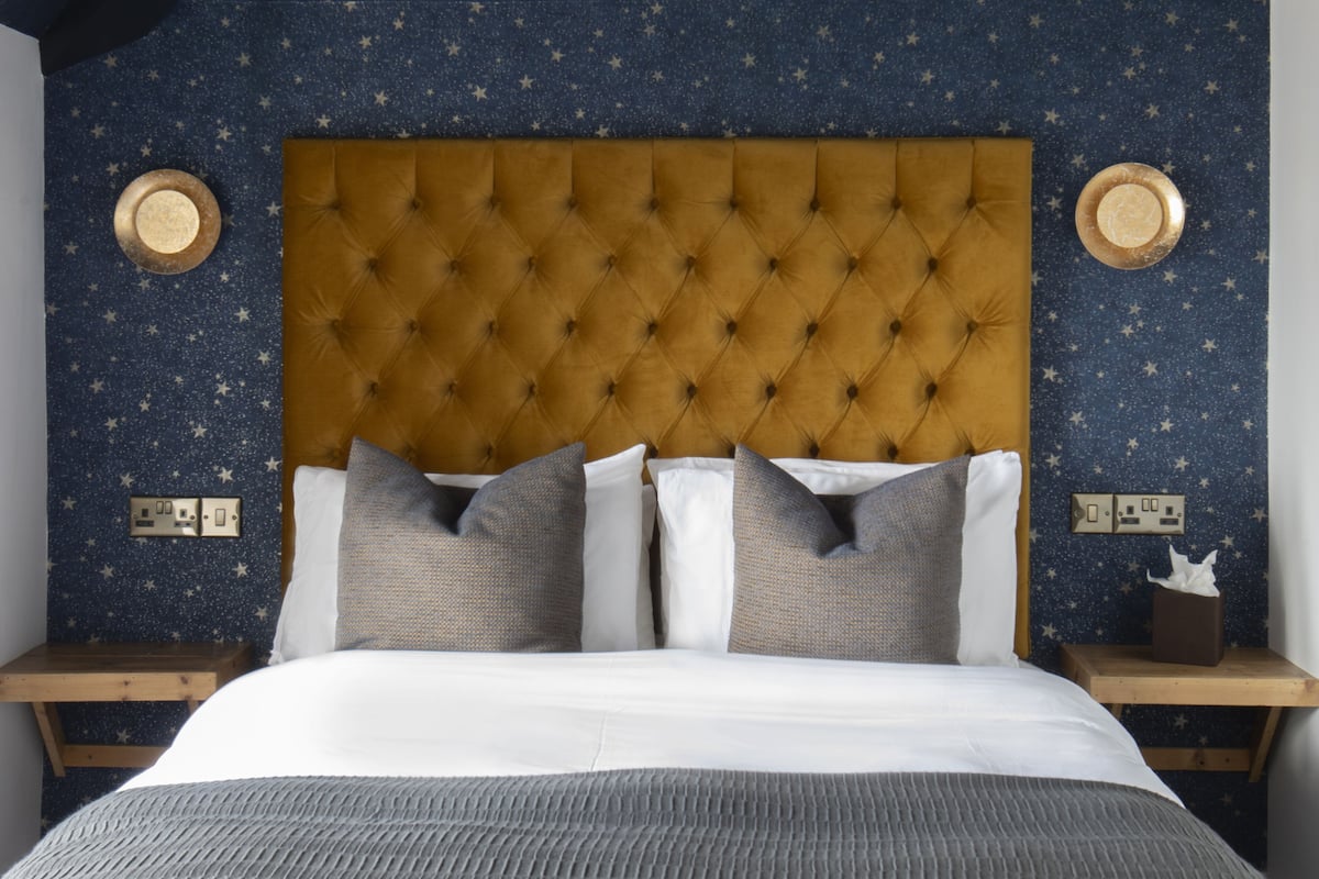 Een slaapkamer met een muur met sterafbeeldingen, een gestuikt hoofdbord en een nachtkastje met een zakdoos.