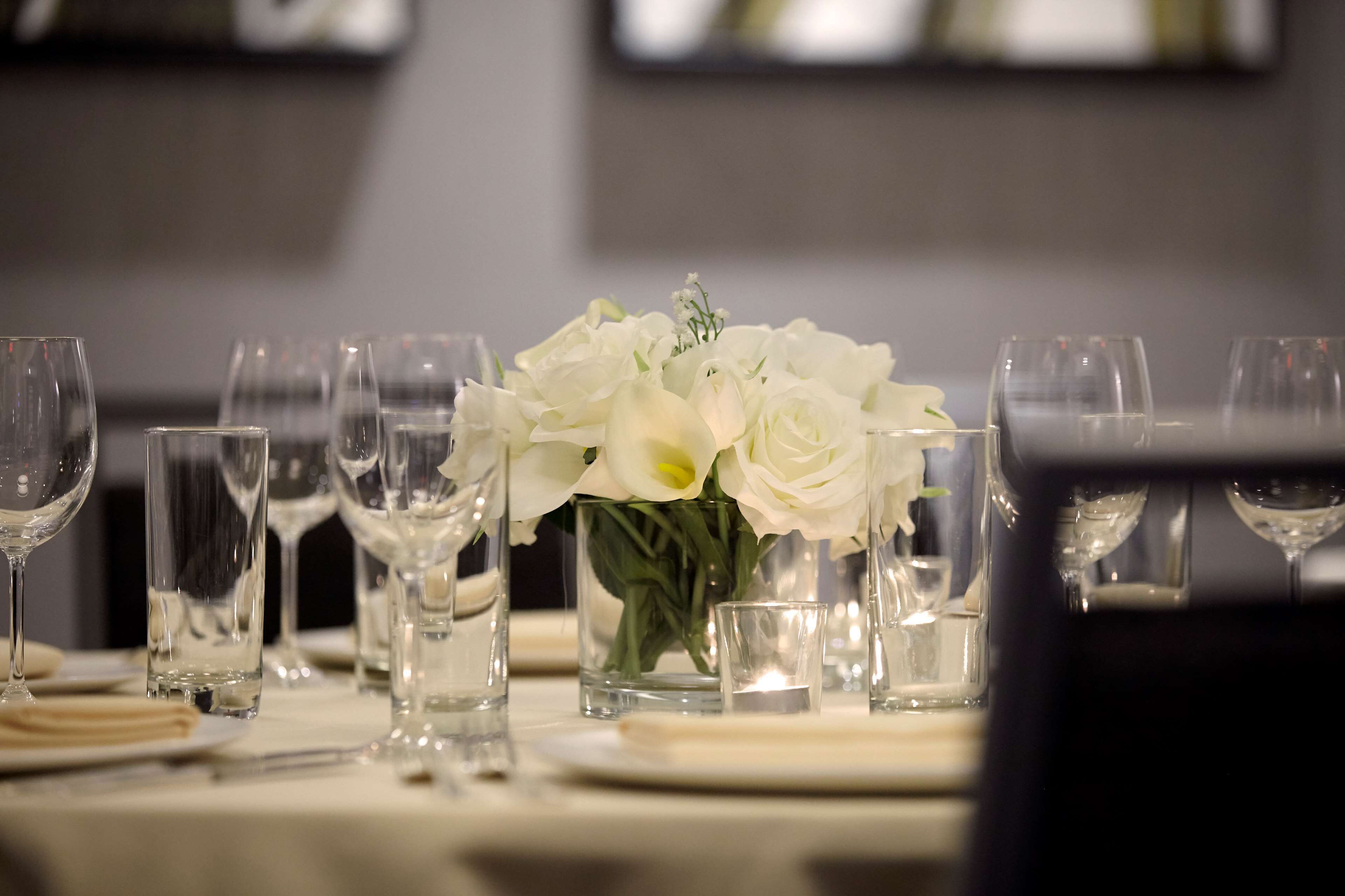 Una mesa dispuesta con vasos transparentes, un pequeño jarrón con flores blancas y una vela.
