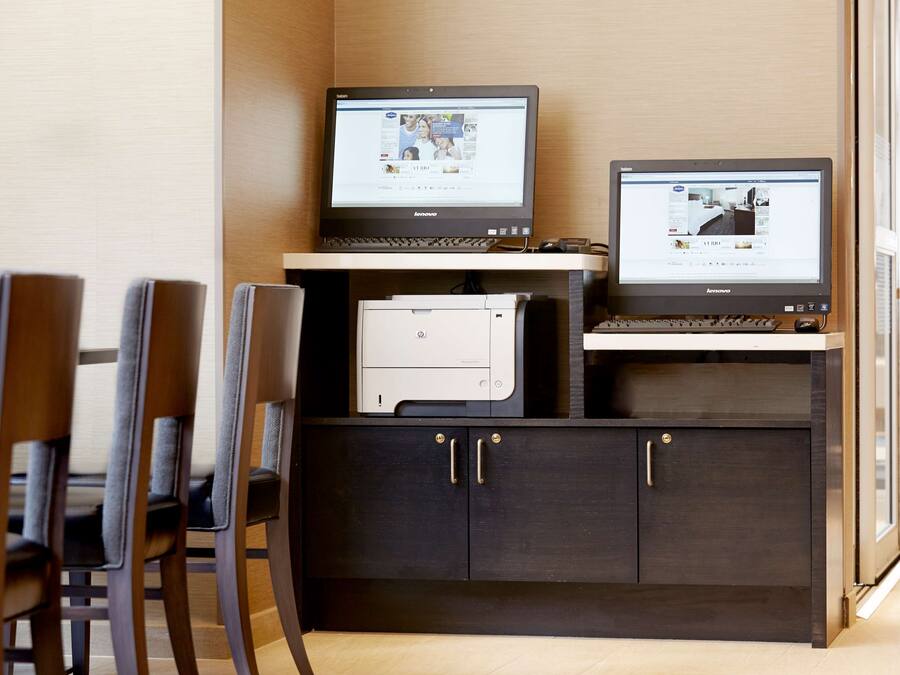 A workspace with two monitors, a printer, and a dark wooden cabinet with handles.