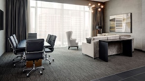 A modern hotel room with a conference table, office chairs, a sofa, and a large window offering a city view. - Hampton Inn Brooklyn/Downtown (Brooklyn)