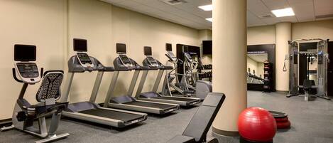 A gym with treadmills, elliptical machines, and a red exercise ball.