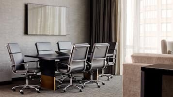 A conference room with a large table, six chairs, a TV mounted on the wall, and a window with curtains.