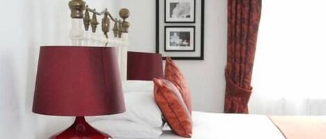 A hotel room with a bed, a red lamp, and framed pictures on the wall.