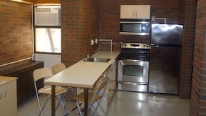 A compact kitchen with a stove, oven, microwave, and refrigerator. There is a window providing natural light and a sink. - University of Toronto - Wilson Hall Residence (Toronto)