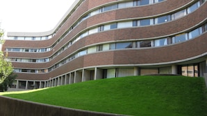 A multi-story building with a curved facade, featuring a series of windows and a grassy area in front. - University of Toronto - Wilson Hall Residence (Toronto)