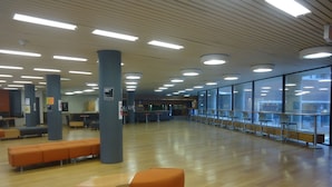 A spacious indoor area with rows of orange and blue seating, large windows, and a high ceiling with recessed lighting. - University of Toronto - Wilson Hall Residence (Toronto)