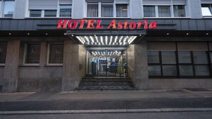 De ingang van HOTEL Astoria, met een moderne gevel, een glazen deur en een trap naar de lobby.