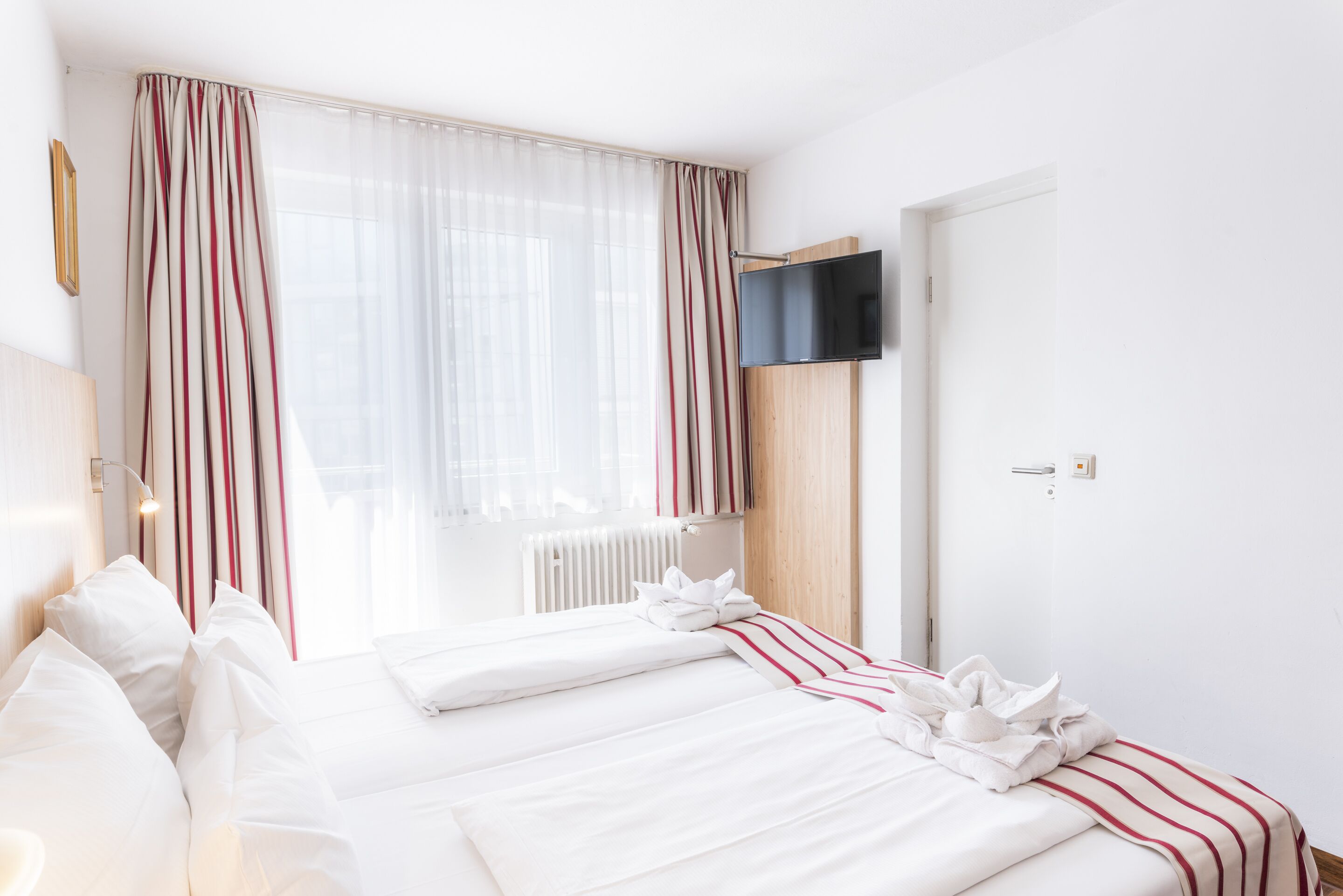 A hotel room with two beds, a TV mounted on the wall, and a window with curtains.