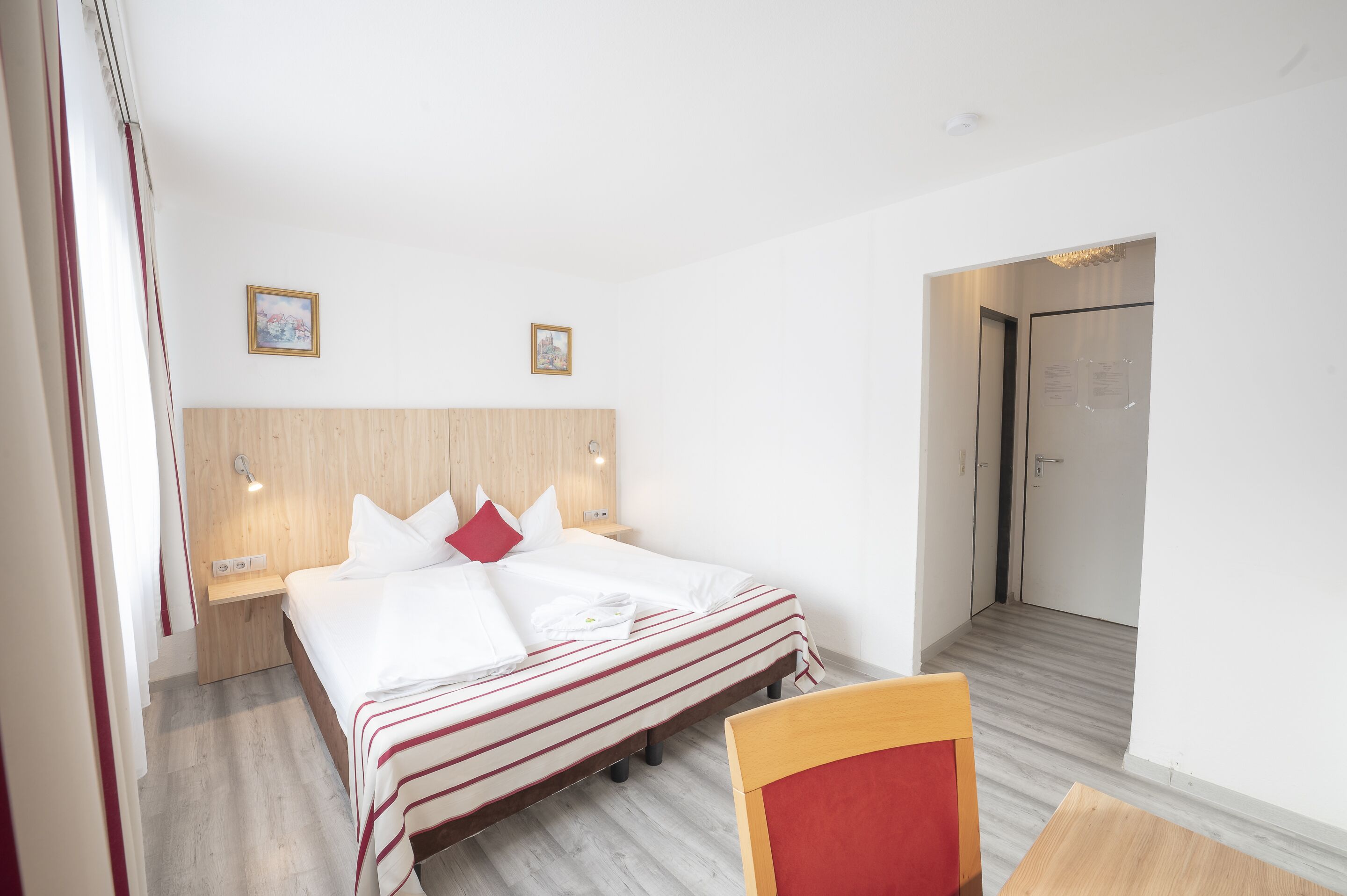 A hotel room with a bed, bedside tables, a wooden headboard, and a door leading to another room.