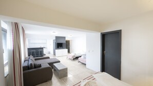 Een moderne, goed verlichte woonruimte met een bank, een lange hocker, een bed en een keuken op de achtergrond.