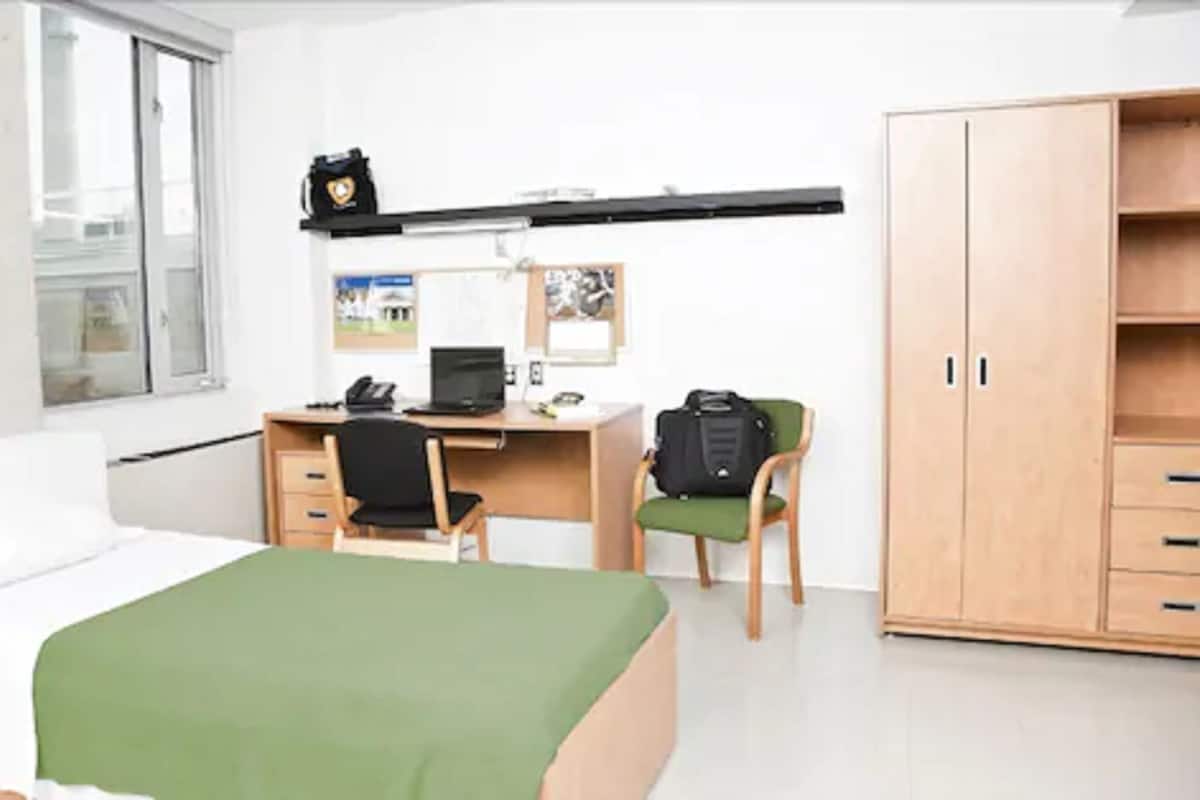 Une chambre à coucher comprenant un lit, un bureau, une chaise, une armoire et une fenêtre.