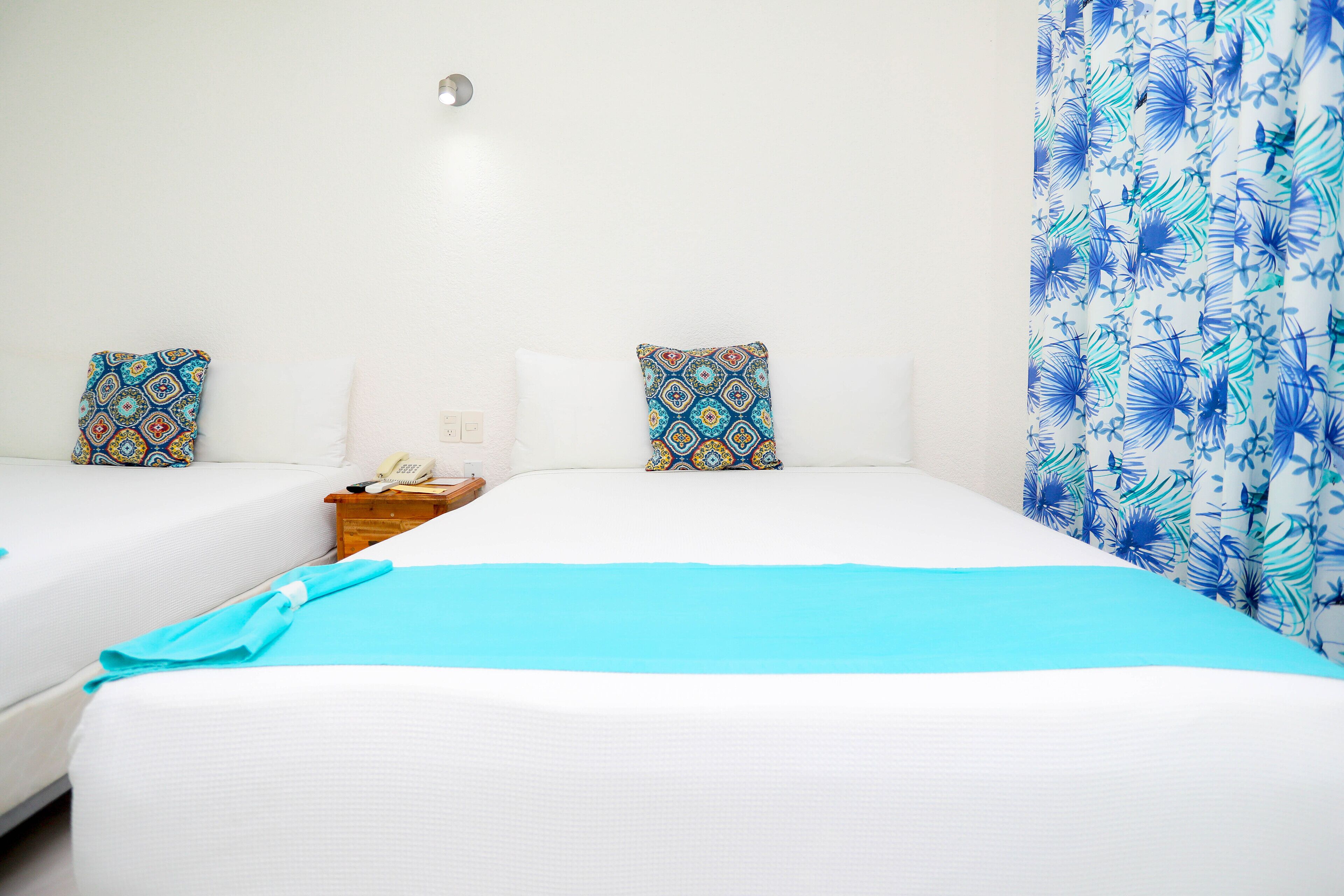 Habitación de hotel con dos camas, una mesita de noche y una cortina estampada.