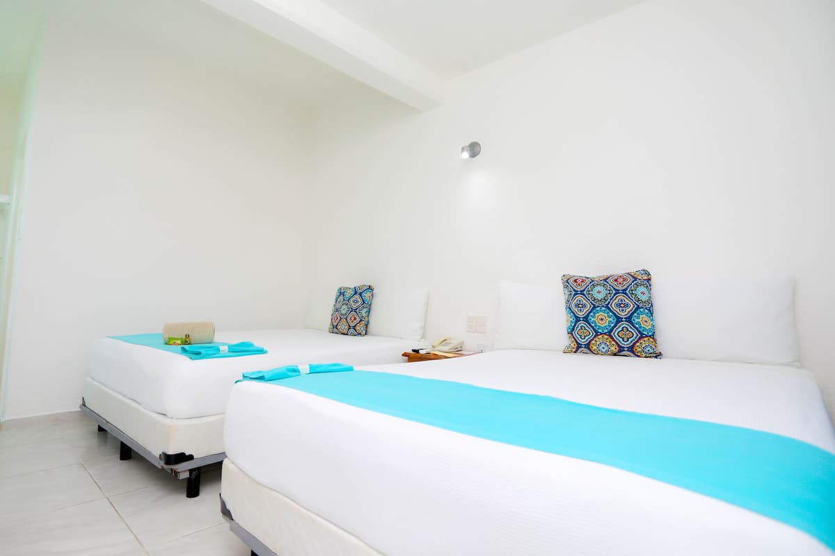 Une chambre d’hôtel avec deux lits, chacun recouvert d’une couverture bleue et agrémenté d’oreillers à motifs.