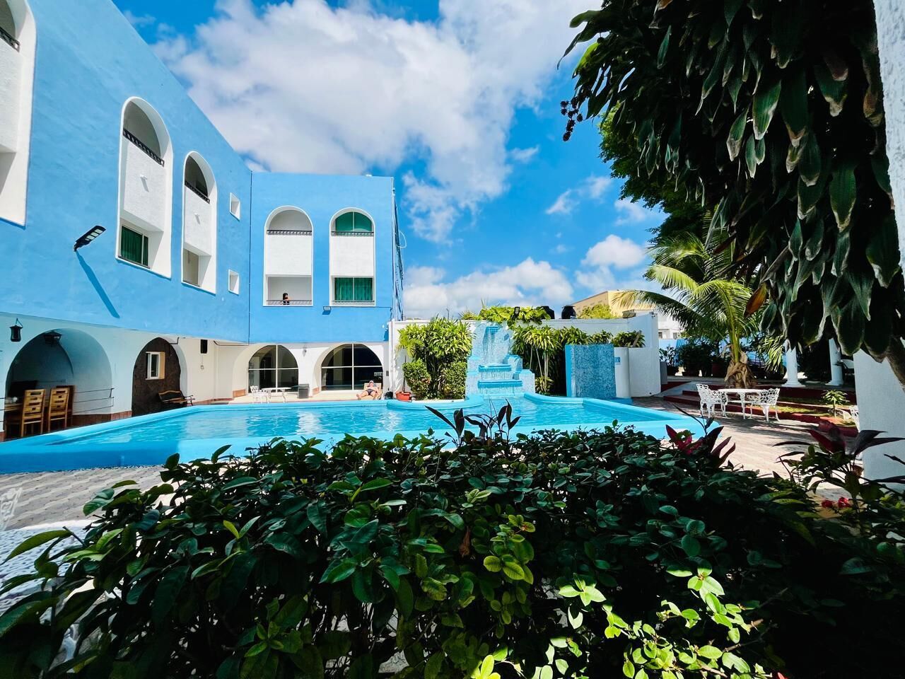A pool area with a blue building, arched windows, and a waterfall feature.