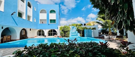 Ein Poolbereich mit einem blauen Gebäude, Bogenfenstern und einem Wasserfall.