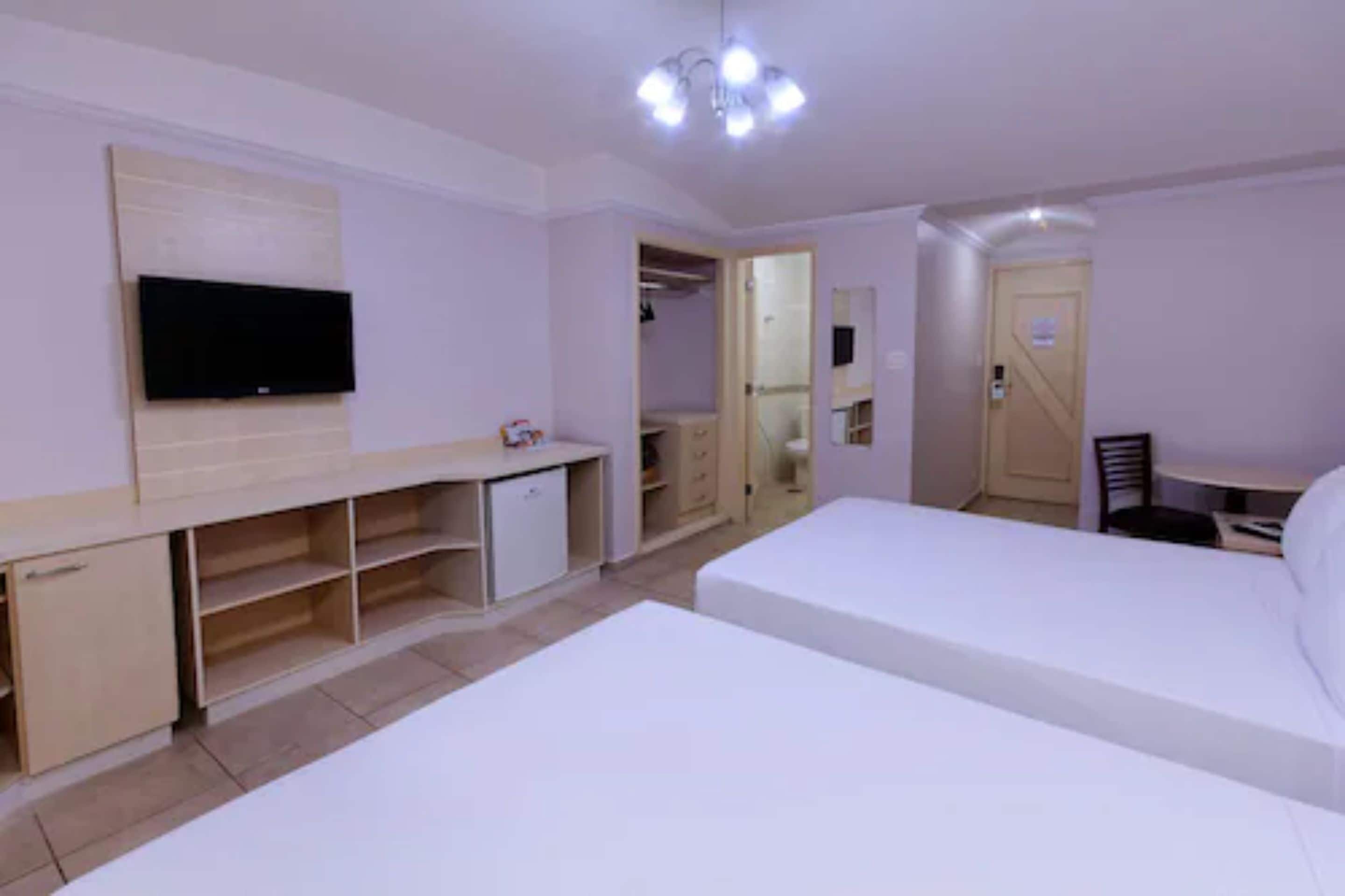 Habitació d'hotel amb llit, televisió, escriptori i armari.
