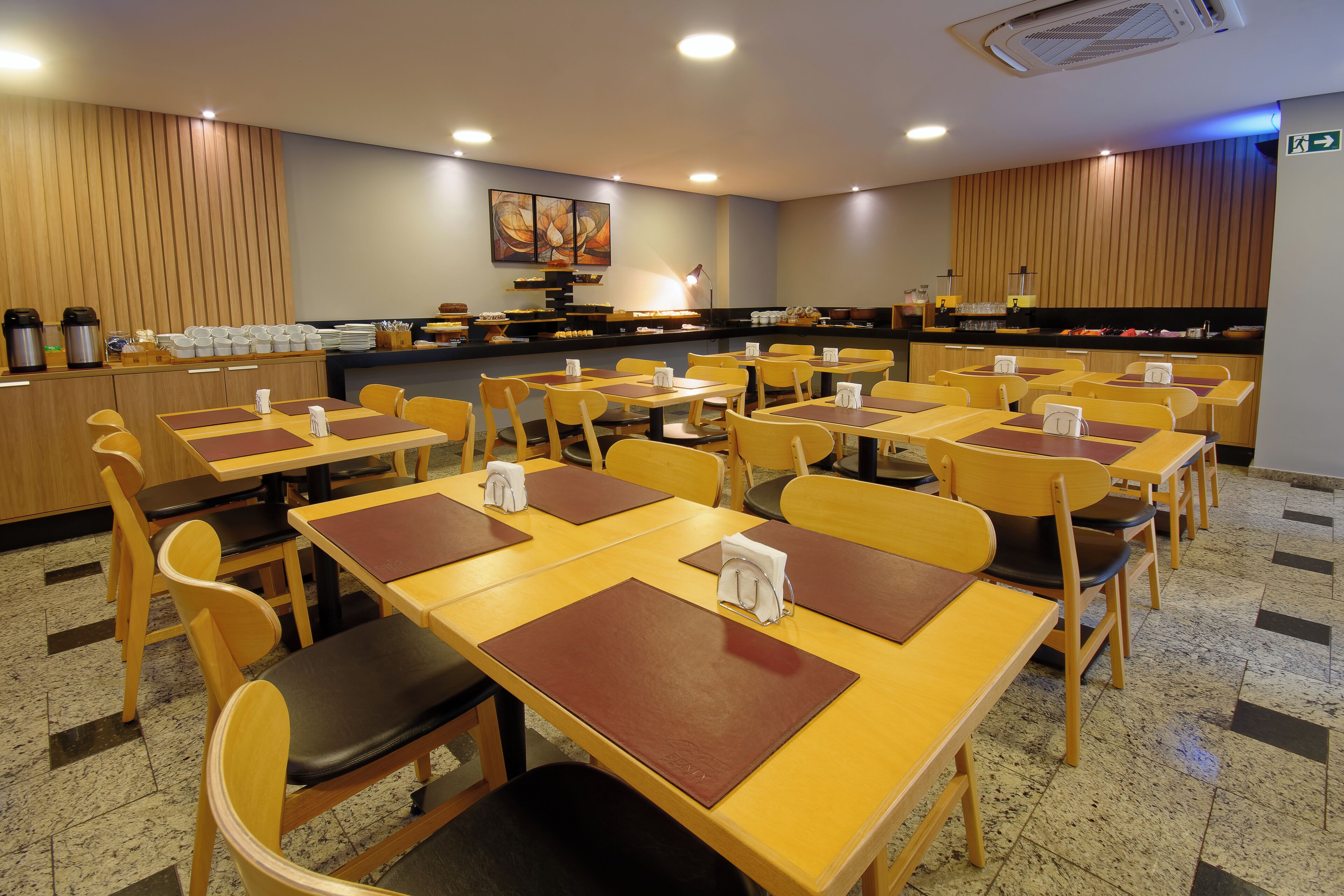 A restaurant with multiple tables and chairs, a counter with food items, and a wall with a painting.
