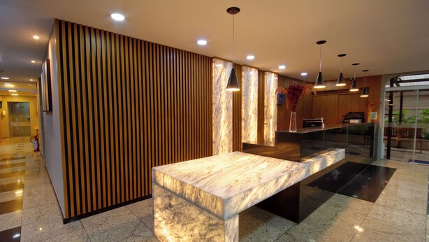 A modern reception area with a marble reception desk, wooden paneling, and pendant lighting. - Fenix Moema (São Paulo)