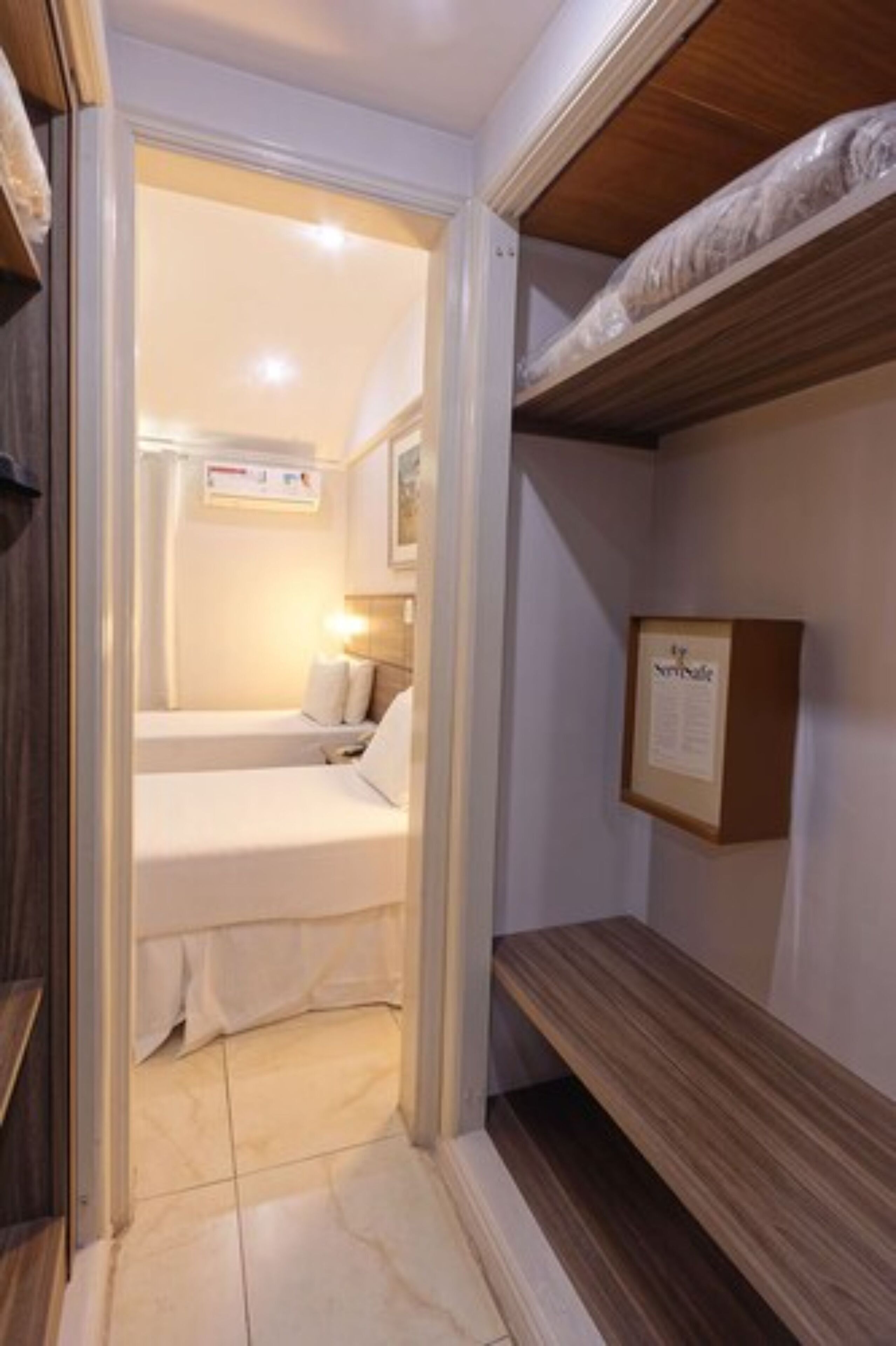A compact hotel room with a small bed, a bedside table, and a framed notice on the wall.