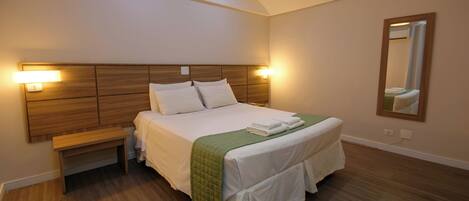 Una cama bien hecha con una manta verde, cabecera de madera y lámparas de noche.