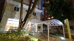 A building with a covered outdoor area, a tree, and a patterned pavement. - Fenix Moema (São Paulo)