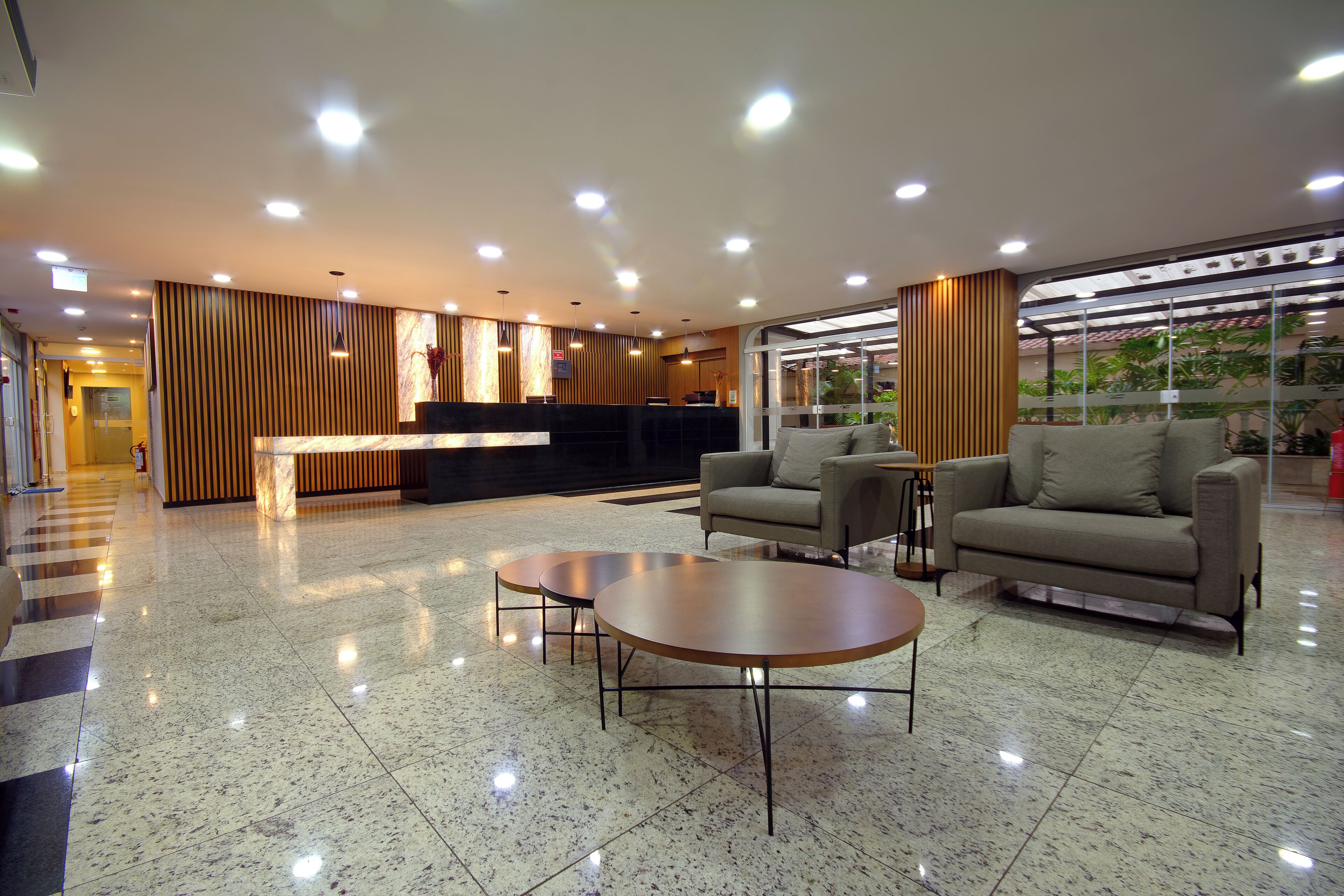 Een moderne hotellobby met een receptiebalie, banken en ronde tafels.