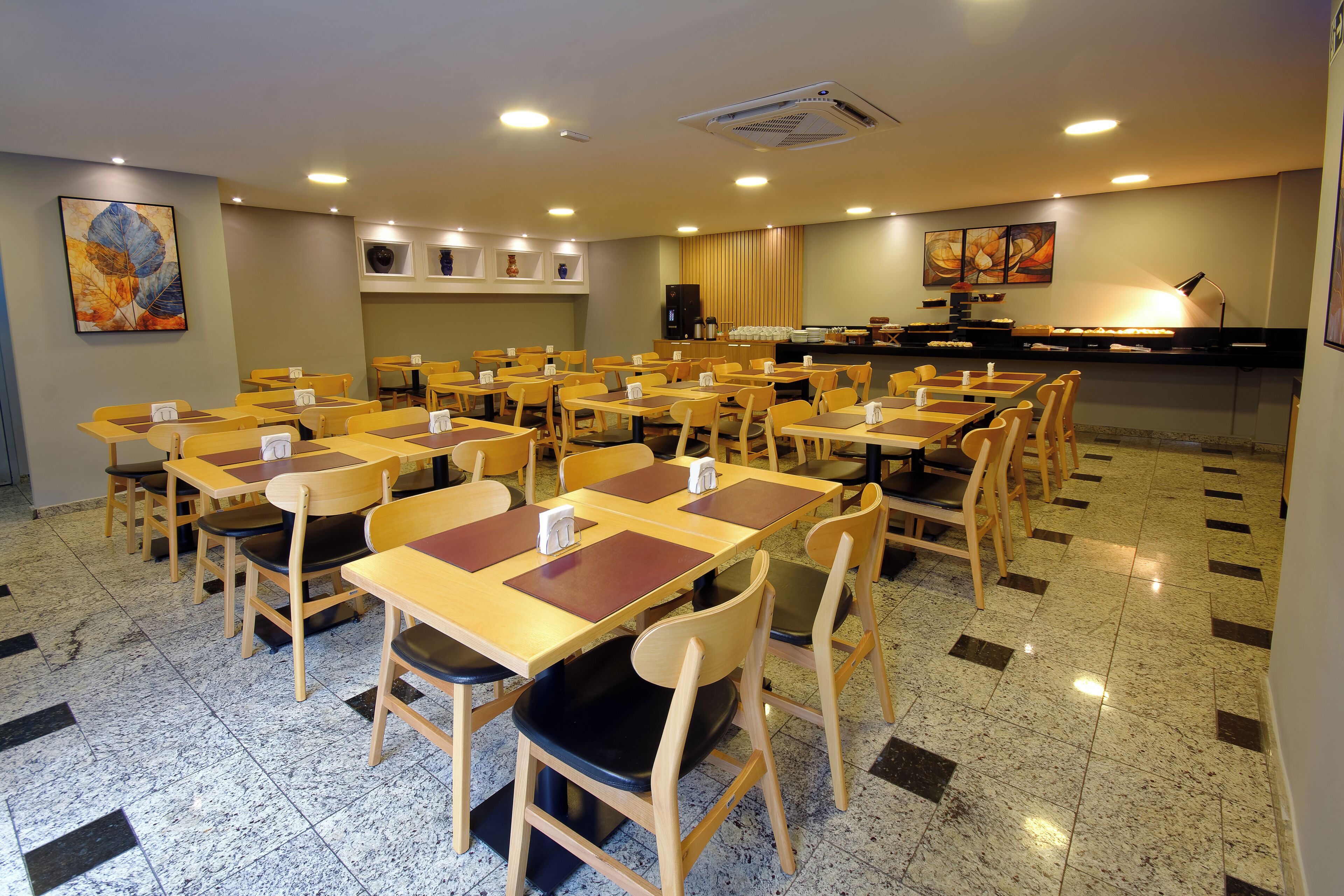 A dining area with multiple tables and chairs, a counter with a coffee machine, and artwork on the walls.