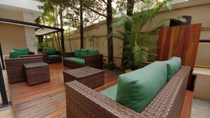 A covered outdoor seating area with wicker furniture and green cushions. - Fenix Moema (São Paulo)