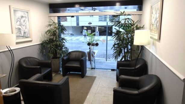 A reception area with black leather chairs, a potted plant, and a view of the street outside. - Paulista Garden Hotel (São Paulo)