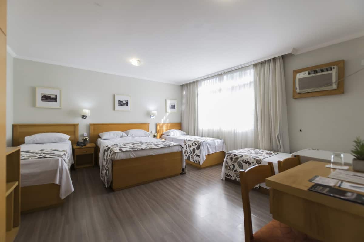 Une chambre d’hôtel avec deux lits, un bureau et une chaise. Il y a des tables de chevet avec des lampes et une fenêtre avec des rideaux.